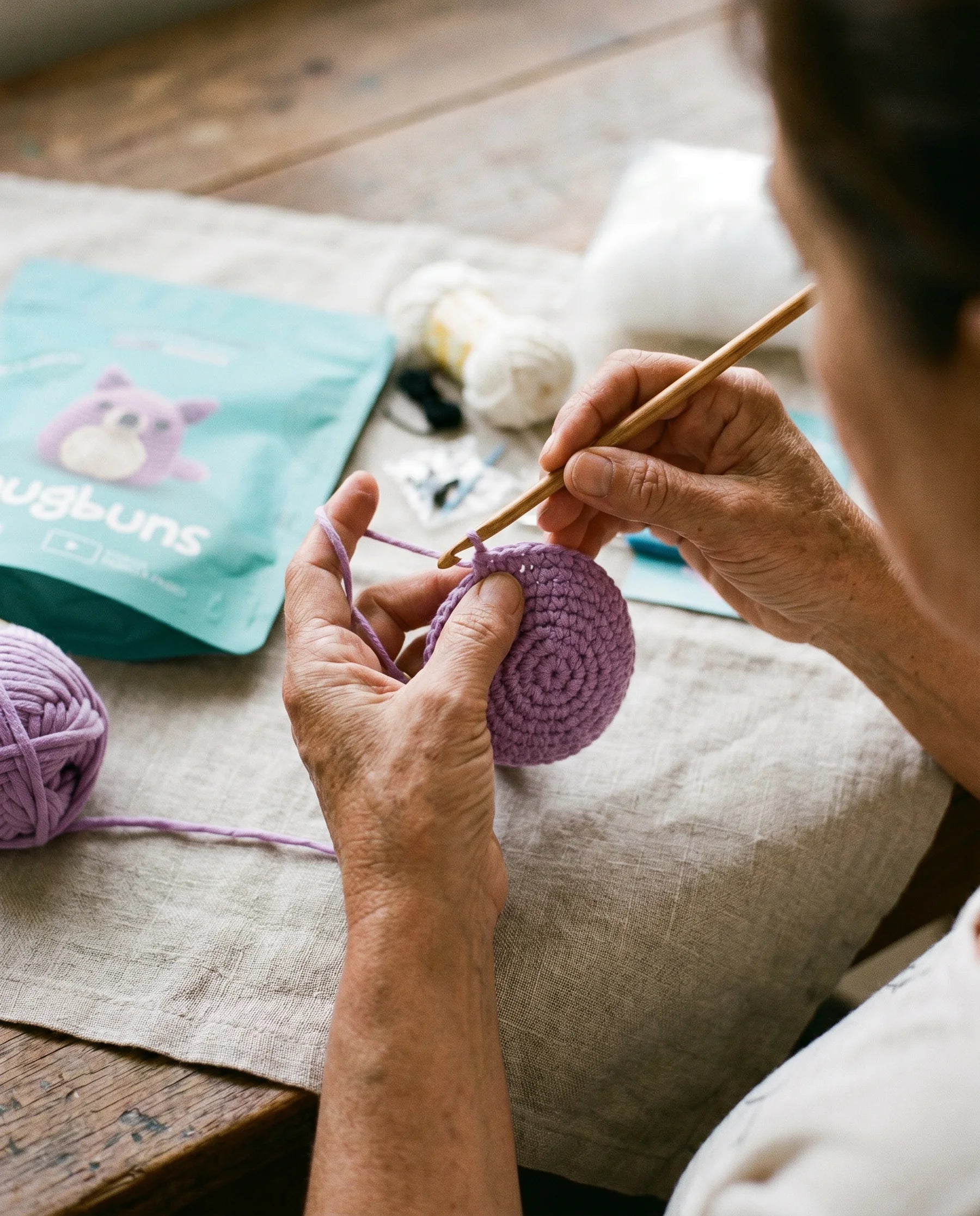 Mãos a trabalhar Wolfie em fio lavanda, kit Snugbuns visível em redor